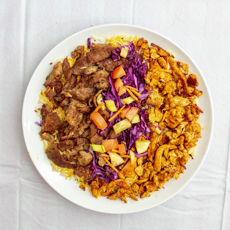 Overhead view of a platter with seasoned rice, grilled meat, spiced chicken, purple cabbage, and chopped vegetables.