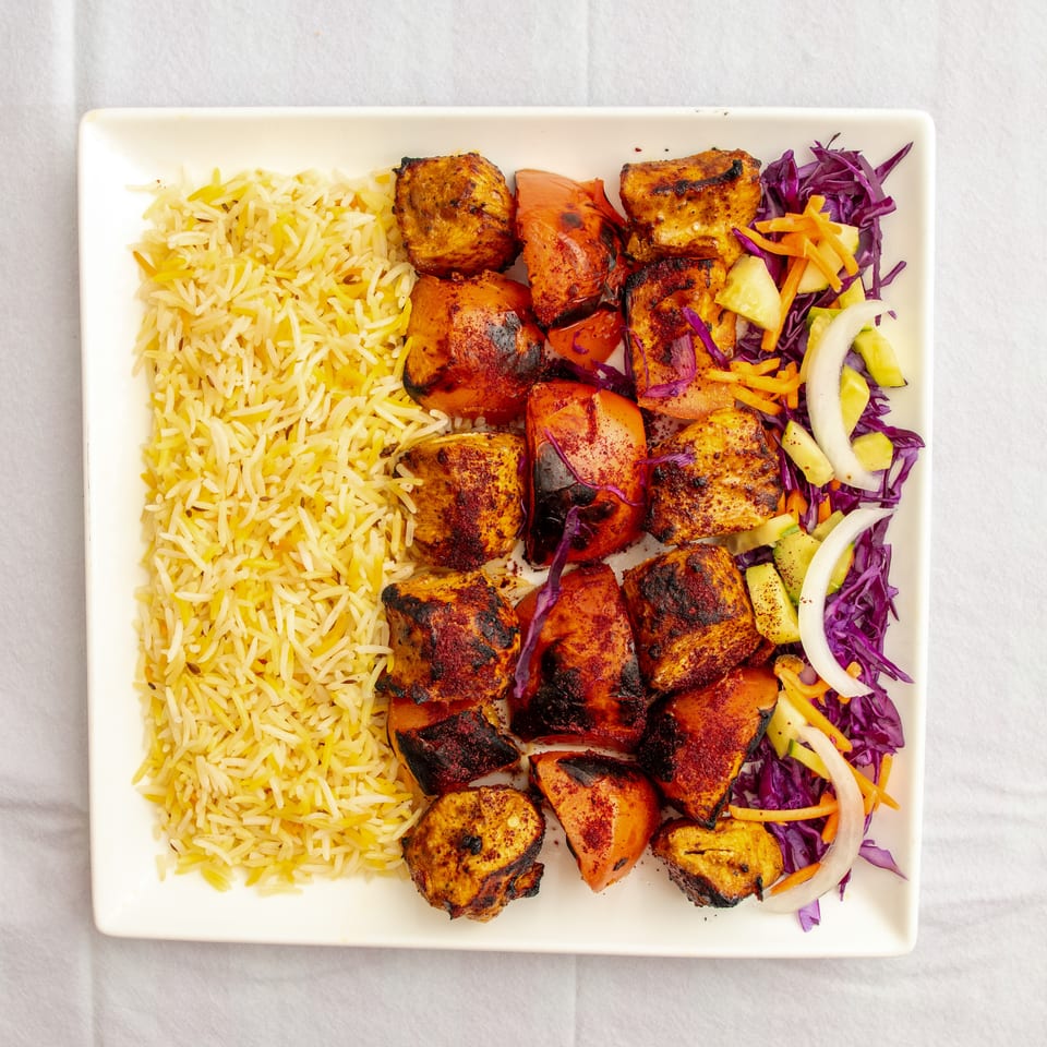 Overhead view of grilled spiced chicken and vegetables with yellow basmati rice and purple cabbage salad on a white plate.