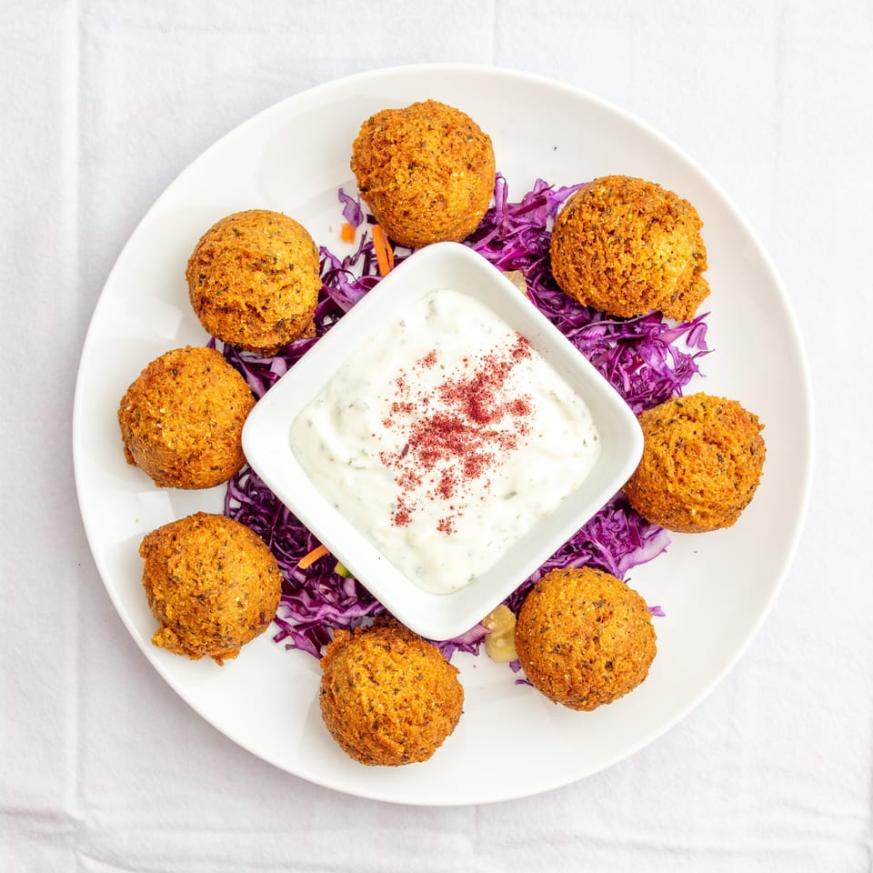 Golden falafel balls arranged around creamy herb sauce, shredded purple cabbage, and carrots on a white plate.